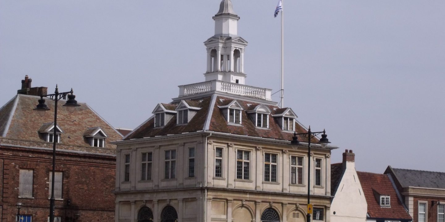 A historic stone customs house with a cupola and clock tower standing beside a quay.