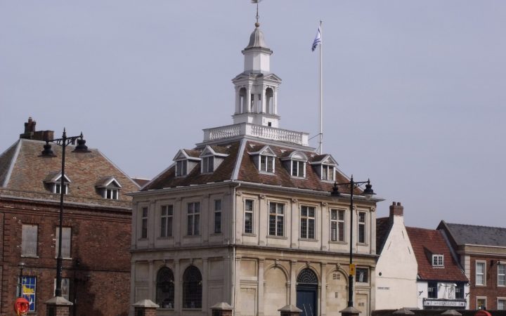 A historic stone customs house with a cupola and clock tower standing beside a quay.