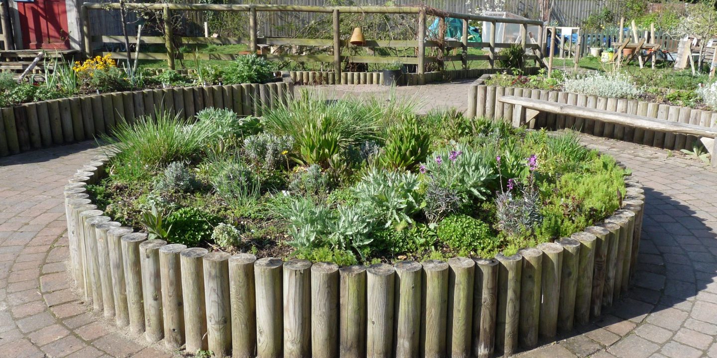 A round raised planting bed edged with timber posts in a paved community garden.
