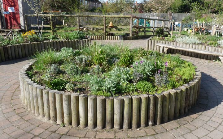 A round raised planting bed edged with timber posts in a paved community garden.