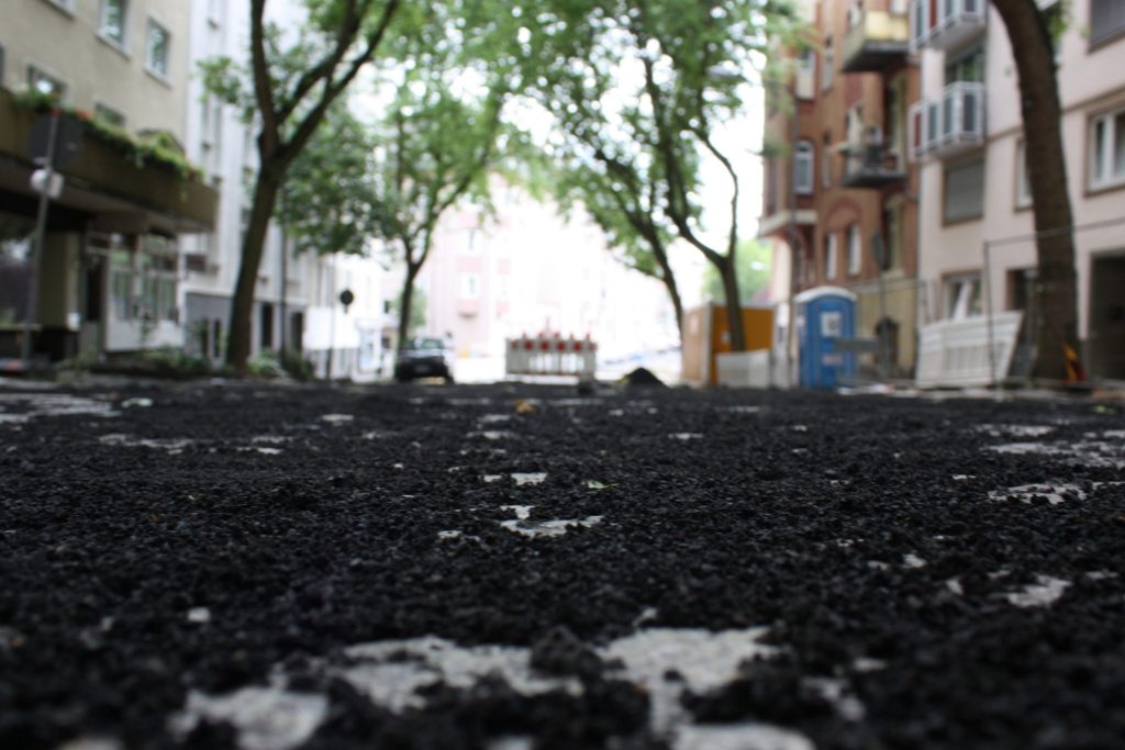 Freshly laid asphalt on a tree-lined city street during resurfacing works.